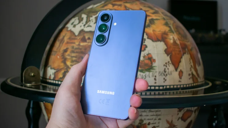 Samsung Galaxy S26 in hand, rear view, in front of a globe