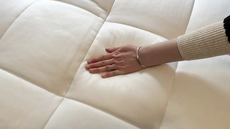 A hand pressing down on the surface of the Simba Natural Hybrid Escape mattress