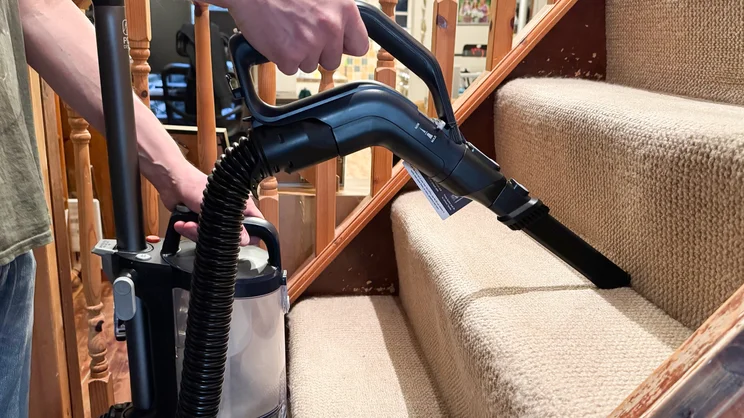 A side view of the Vax LiftOut Multi Pet Design Upright Vacuum in use. Its crevice tool is being used to clean stairs