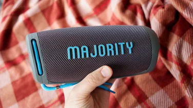 The Majority Move M3 portable Bluetooth speaker being held in a hand above a tartan quilt