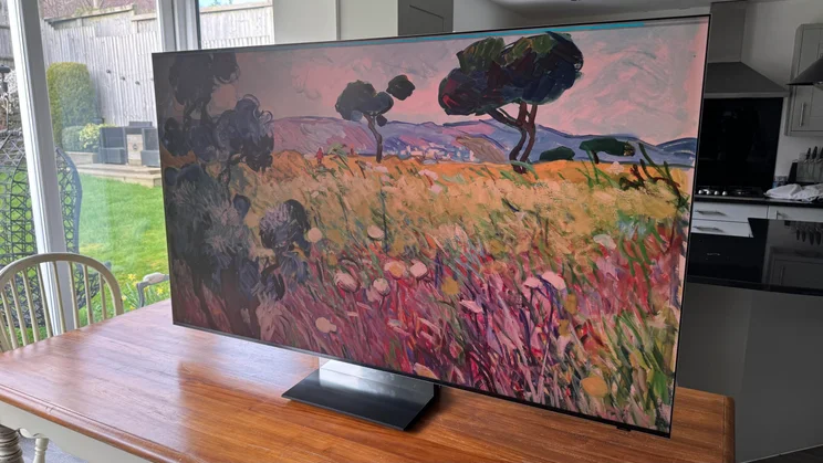 Right view of the Samsung R95H Micro LED TV on a wooden table in a conservatory displaying a digital artwork of a natural landscape