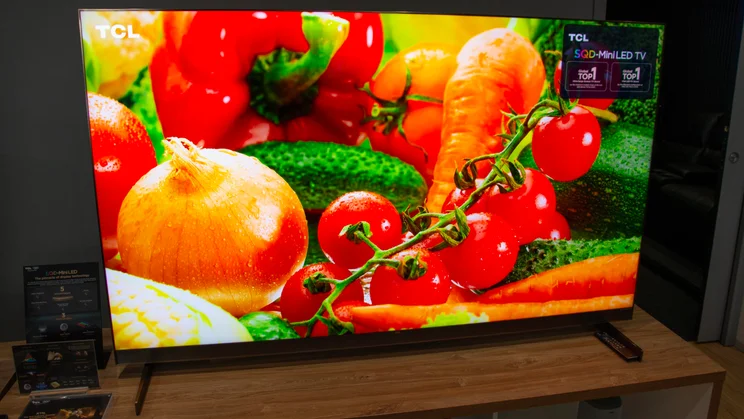 The TCL X11L SQD Mini LED TV on a wooden table displaying an image of fresh vegetables