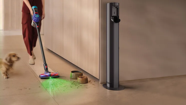 A lifestyle image of the Dyson V10 Konical cleaning up spilled pet food , alongside a small dog and the Auto-empty Dok