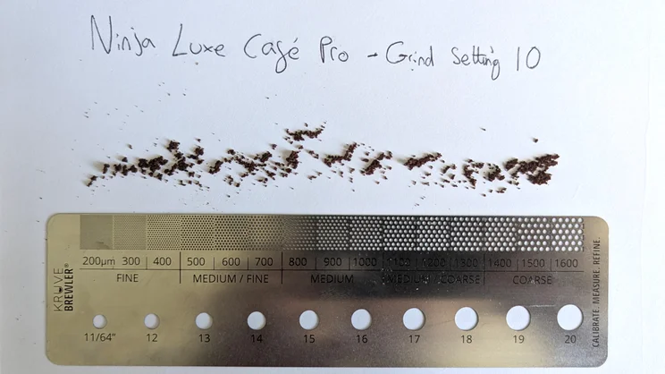 A bird's eye view of ground coffee being measured against the Kruve Brewler. Handwriting above reads "Ninja Luxe Cafe Pro - Grind setting 10"
