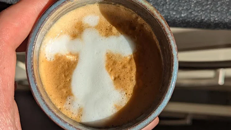 A bird's eye view of a cup of coffee, with latte art depicting a figure with arms outstretched