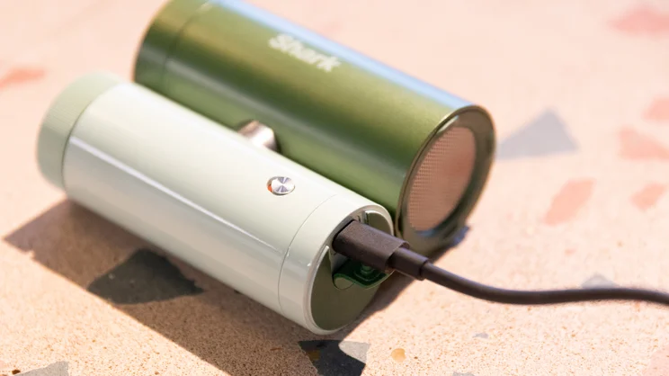 The Shark ChillPill portable fan lying flat on a table, a black USB-C cable plugged into its charging port