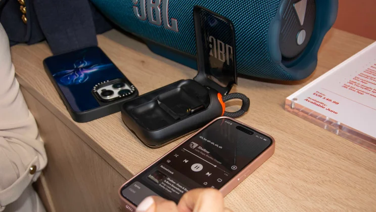 The case of the JBL EasySing Mic Mini open on a table with a music app open on a phone nearby