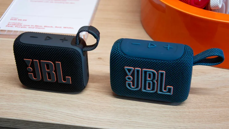 A black JBL Go 4 (left) next to a blue JBL Go 5 (right) on a wooden table