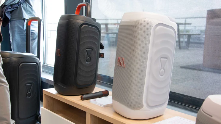 The JBL PartyBox 330 (left) and JBL PartyBox 130 (right) on a wooden table in front of a balcony window