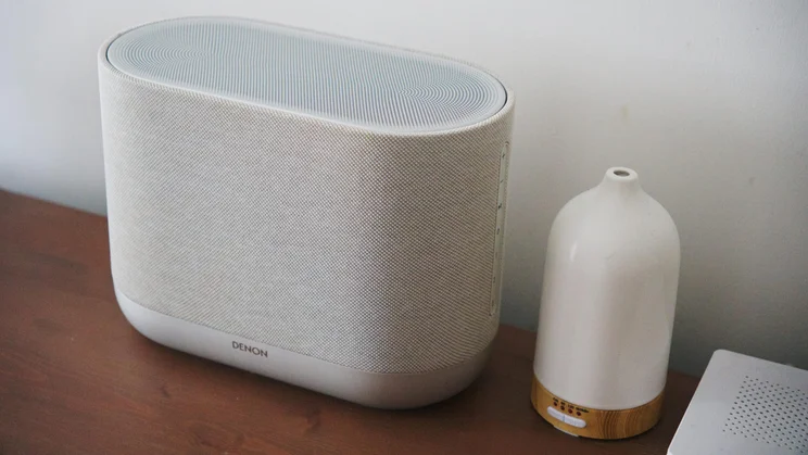 Angled view of the Denon Home 400 wireless speaker alongside a scent diffuser on a wooden table