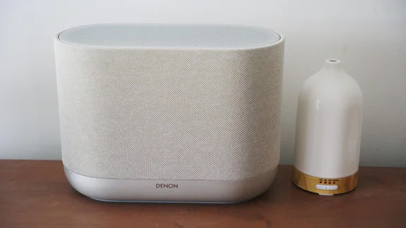 Front view of the Denon Home 400 wireless speaker alongside a scent diffuser on a wooden table