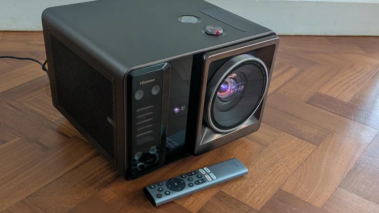 Front view of the Hisense XR10 laser projector facing to the right with its remote control in front of it