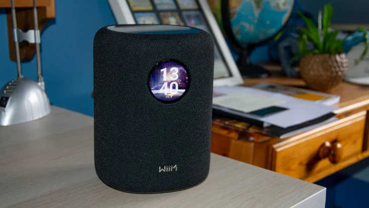 The WiiM Sound speaker on a desk displaying the digital clock on a cosmic wallpaper
