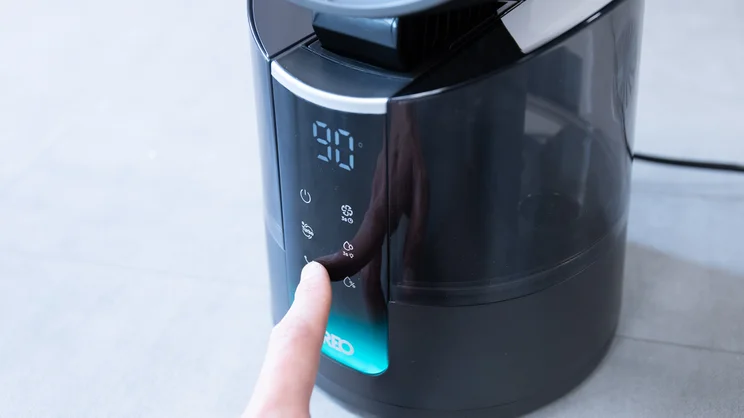 The Dreo TurboCool Misting Fan 516S on the floor of an office. A hand is operating its control panel