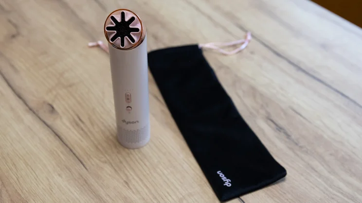The Dyson HushJet Mini Cool fan standing on an office table, alongside its drawstring pouch
