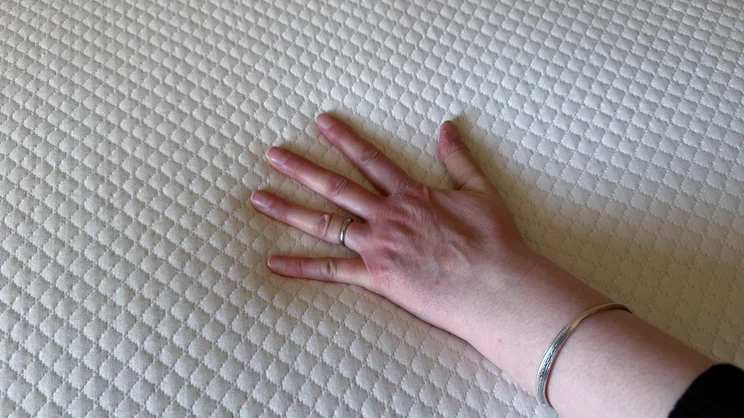 A hand pushing down on the Simba Cool Foam mattress topper's surface