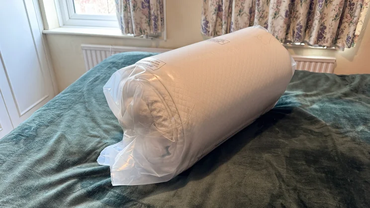The Simba Cool Foam mattress topper rolled up and vacuum sealed, on a mattress