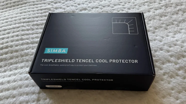 A bird's eye view of the Simba TripleShield Tencel Cool mattress protector packaged in its box, on top of a mattress