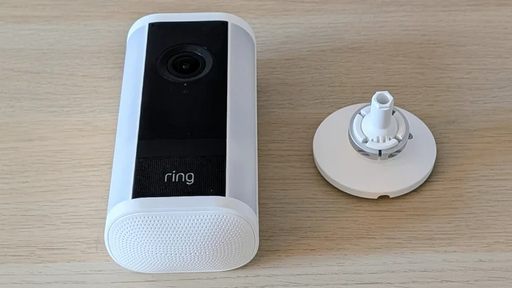 The Ring Spotlight Cam Pro Plug-In (2nd gen) laid on its back on a wood surface with its mounting bracket next to it