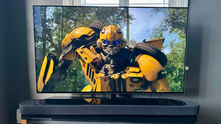 Front view of the Bose Lifestyle Ultra Soundbar on a TV stand in front of a TV showing the film Bumblebee