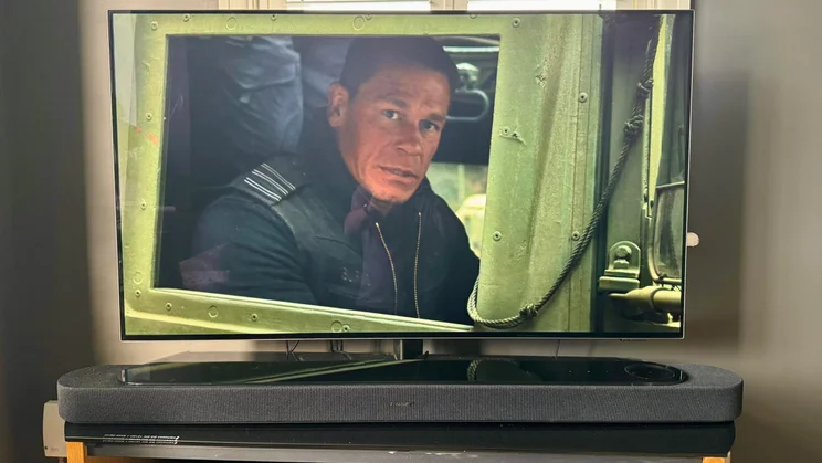 Front view of the Bose Lifestyle Ultra Soundbar on a TV stand in front of a television showing John Cena in Bumblebe