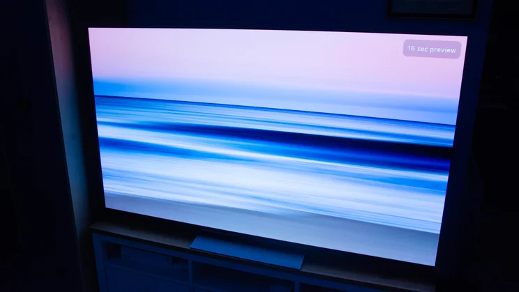 The 65in LG C6 OLED TV on a wooden stand in a dark room displaying a screensaver of a sea