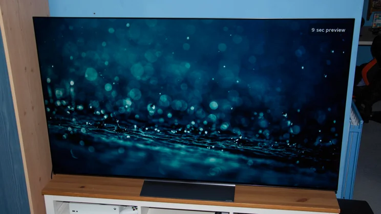 The 65in LG C6 OLED TV on a wooden stand displaying an image of raindrops falling