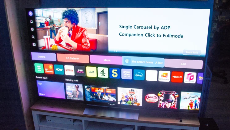 The 65in LG C6 OLED TV on a wooden stand displaying a pre-production version of the homepage of webOS 26
