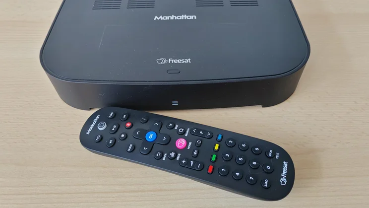 The Manhattan S4-R Freesat TV Recorder on a wooden table with the remote control in front of it