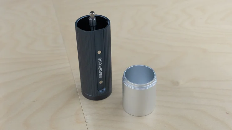 The AeroPress Manual Coffee Grinder and grounds container separated, placed side-by-side on a table in an office