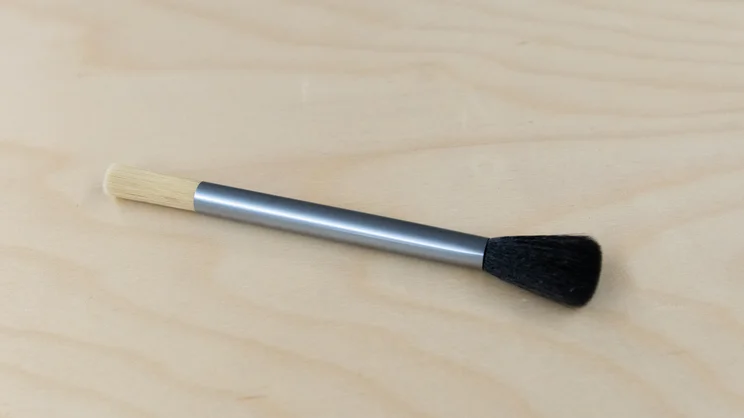 The AeroPress Manual Coffee Grinder's double-sided cleaning brush on a table