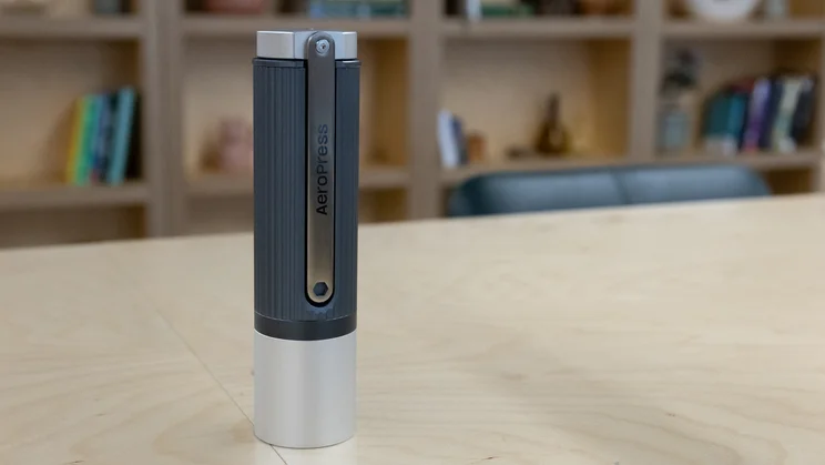 The AeroPress Manual Coffee Grinder, with its handle stored, on a table in an office