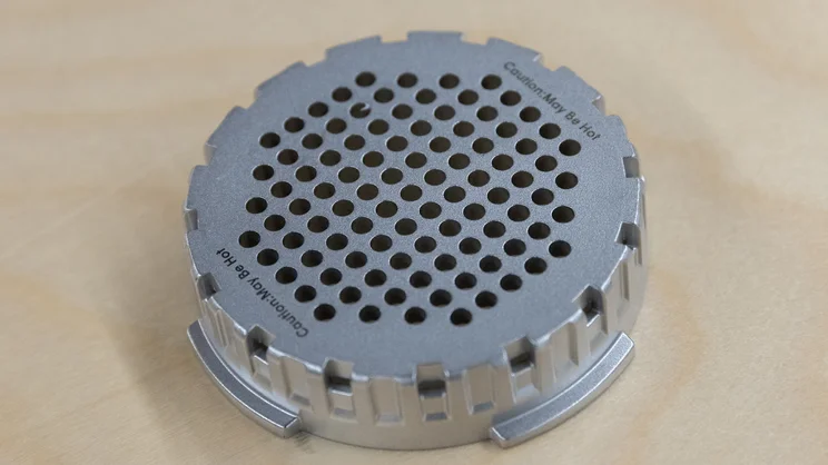 A closeup of the AeroPress Steel coffee maker's filter cap on a table in an office