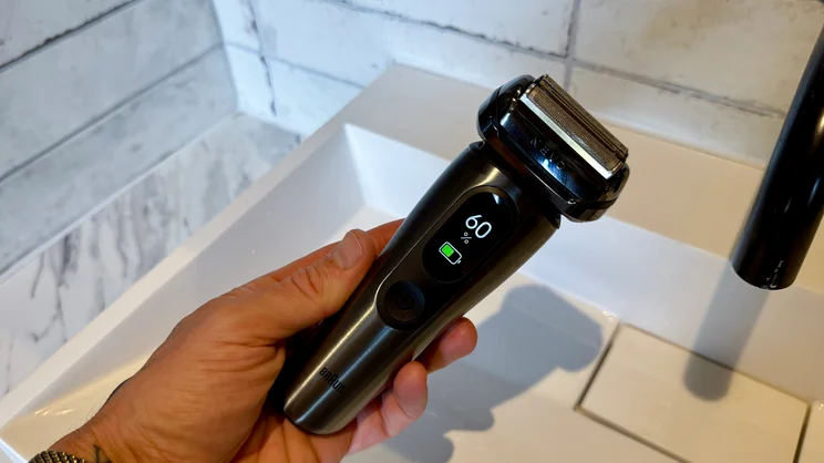 The Braun Nevo electric shaver in a hand, held over a sink. Its digital display shows the shaver's battery life at 60%