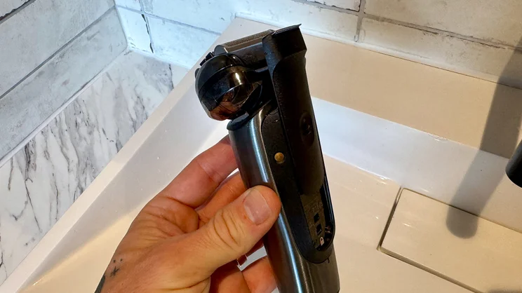 A side view of the Braun Nevo electric shaver in a hand, held over a sink.