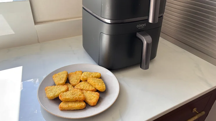 A plate of cooked hash browns alongside the Cosori Turbo Tower air fryer