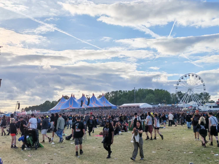 A big crowd with tents and a ferris wheel in the distance