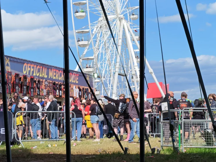 A merch tent and ferris wheel with people queueing