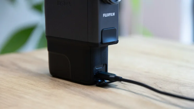 A closeup of the Instax Mini Evo Cinema's USB-C charging port. A black cable has been inserted
