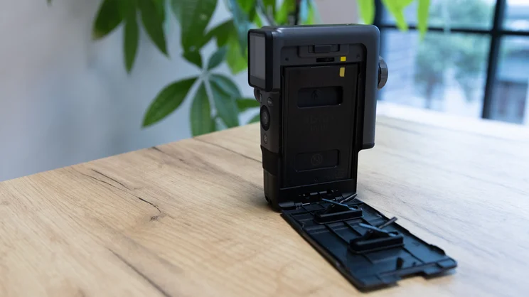 The Instax Mini Evo Cinema on a table in an office. The film compartment is open and a pack of film has been inserted