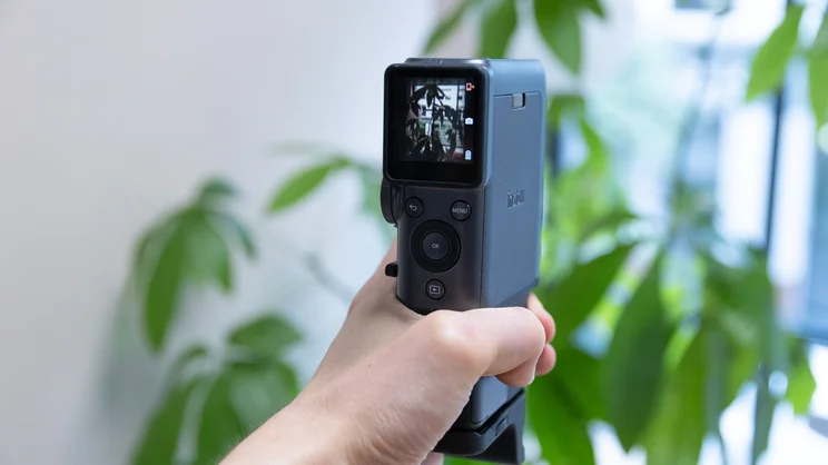 The Instax Mini Evo Cinema held in a hand, pointed at a large potted plant