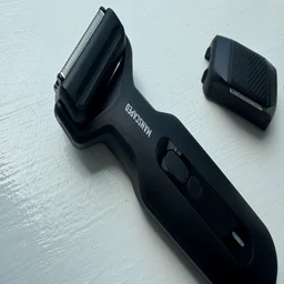 The Manscaped Chairman Plus electric shaver, with foil head attached, on a windowsill, alongside its precision tool