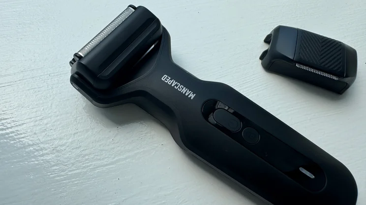 The Manscaped Chairman Plus electric shaver, with foil head attached, on a windowsill, alongside its precision tool