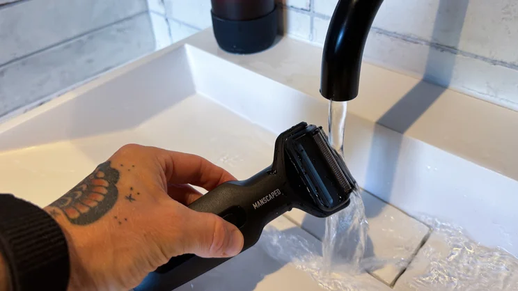 The Manscaped Chairman Plus electric shaver being run under the tap of a bathroom sink