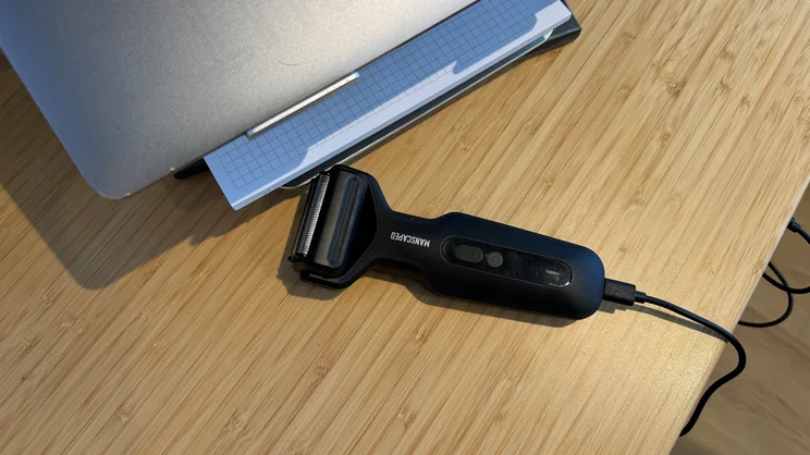 The Manscaped Chairman Plus electric shaver plugged in and charging, on a desk