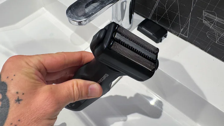 The Manscaped Chairman Plus electric shaver, with foil head attached, in a hand over a sink