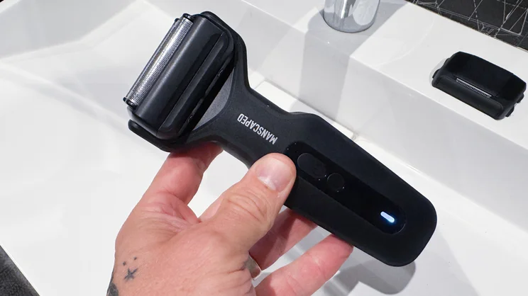 The Manscaped Chairman Plus electric shaver, with foil head attached, in a hand over a sink