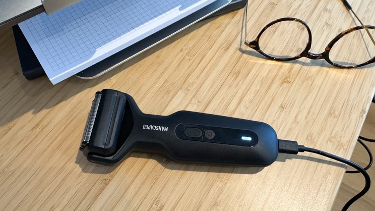 The Manscaped Chairman Plus electric shaver plugged in and charging on a desk