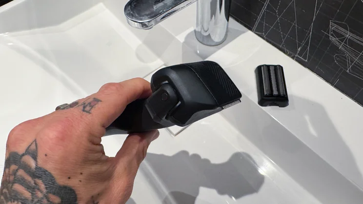 The Manscaped Chairman Plus electric shaver, with its precision tool head attached, in a hand over a sink