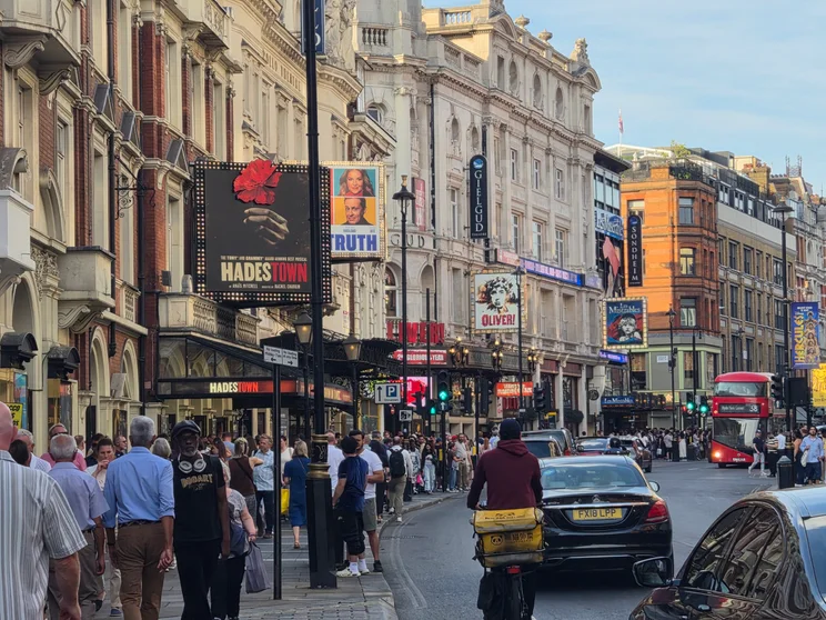 A busy London street with signs for musicals